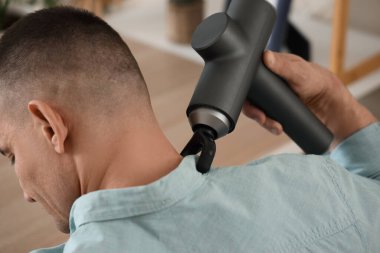 Evde boynuna vurmalı masaj aleti ile masaj yapan genç bir adam.