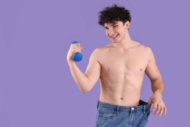 Mor arka planda dambılı bol kotlu yakışıklı genç sporcu. Kilo verme konsepti