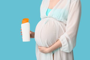 Mavi arka planda güneş kremi şişesi olan hamile bir kadın.