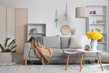 Yumuşak kanepe, kahve masası ve açık oturma odasında narsisli çiçekler.