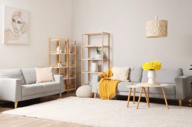 Rahat bir kanepe, raf ünitesi ve oturma odasında vazo dolusu narsist çiçekli kahve masası.