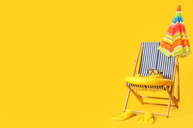 Renkli şemsiyeli, plaj aksesuarlı ve sarı arka planlı çizgili sandalye.