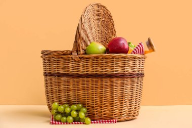 Bej arka planda piknik için lezzetli yiyecekler ve meyve suyu içeren hasır sepet.