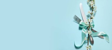 Mavi arkaplanda çiçek açan ağaç dalına sahip gümüş çatal bıçak seti.