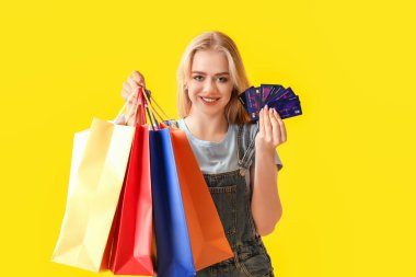Sarı arka planda alışveriş torbaları ve kredi kartları olan genç bir kadın.