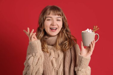 Güzel genç bir kadın elinde bir fincan sıcak çikolata ve kırmızı arka planda tarçın tutuyor.