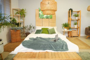 Yatak odasının içinde yeşil bitkiler, raf üniteleri ve yatağın üstünde dizüstü bilgisayar var.