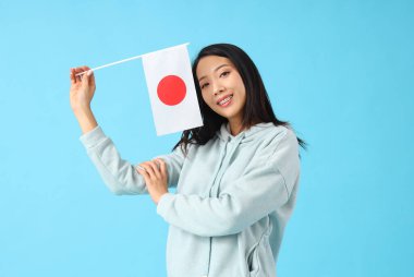 Mavi arka planda Japon bayrağı olan genç bir Asyalı kadın.