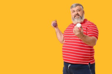 Sarı arka planda halterli, kilolu, olgun bir adam. Kilo verme konsepti