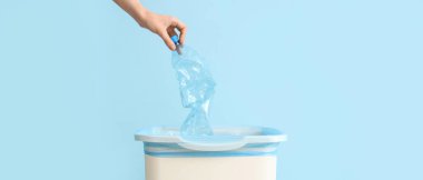 Kadın eli açık mavi arka planda plastik şişeyi çöp kutusuna atıyor. 