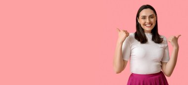 Gülümseyen genç kadın pembe arka planda mesaj için yeri olan baş parmak hareketi gösteriyor