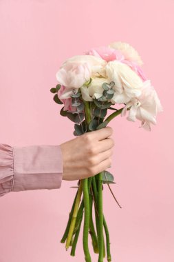 Güzel bir buket ranunculus çiçeğiyle kadın eli ve pembe arka planda okaliptüs.