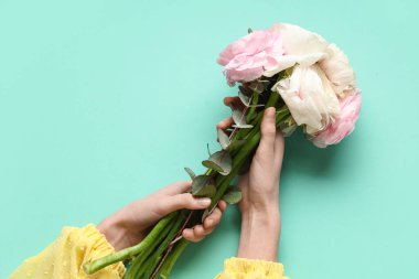 Güzel bir buket ranunculus çiçeği ve turkuaz arka planda okaliptüs olan kadın elleri.