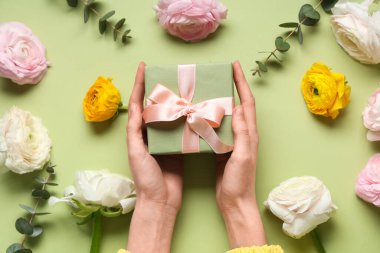 Hediye kutusu olan kadın elleri, güzel ranunculus çiçekleri ve yeşil arka planda okaliptüs.