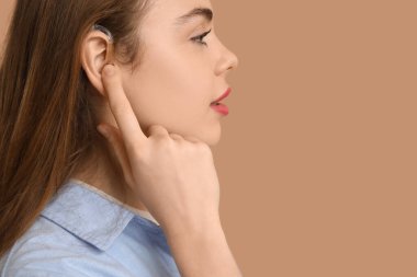 Kahverengi arka planda işitme cihazı olan güzel genç bir kadın.