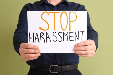 Yeşil arkaplanda DUR HARASSMENT yazılı kağıt tutan işadamı, yakın plan