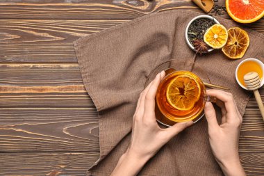 Taze portakal çayı ve ahşap arka planda bal tutan kadın elleri.