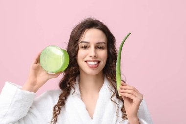 Güzel genç bir kadın pembe arka planda aloe vera ve bir kavanoz krema tutuyor.
