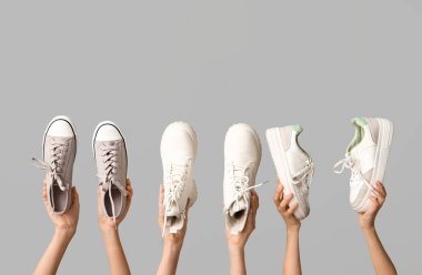 Şık spor ayakkabıları ve gri arka planda beyaz deri çizmeleri olan kadın elleri.