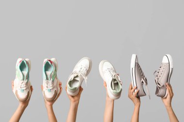 Gri arka planda farklı şık spor ayakkabıları olan kadın elleri.