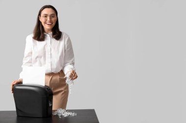 Sekreter arka planda belgeyi kağıt öğütücüsünde imha ediyor