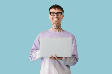 Mavi arka planda dizüstü bilgisayar kullanan gözlüklü genç bir adam.