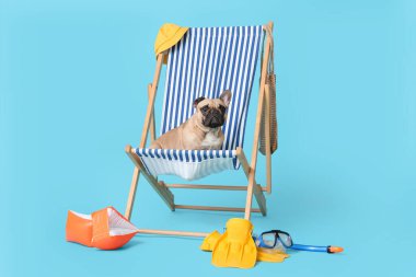 Mavi arka planda güverte sandalyesinde yüzme aksesuarlarının yanında oturan sevimli Fransız bulldog.