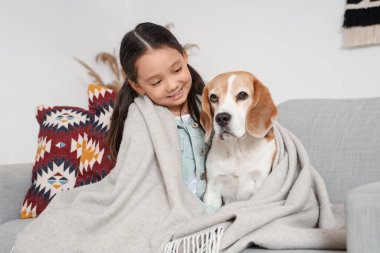 Evdeki kanepede oturan Beagle köpeği ve ekoseli şirin Asyalı kız.