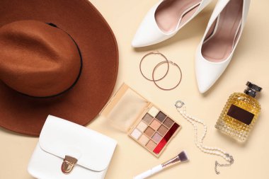 Bir şişe parfüm, göz falı, bej arka planda çanta ve aksesuarlar.