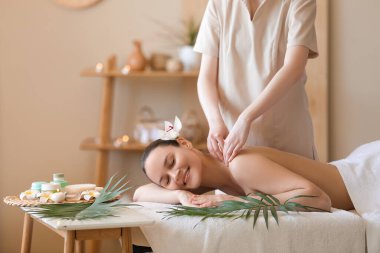 Mutlu genç bir kadın spa salonunda omuzlarına masaj yaptırıyor.