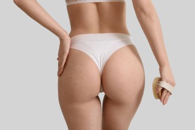 Young woman with massage brush and scrub on butt against white background