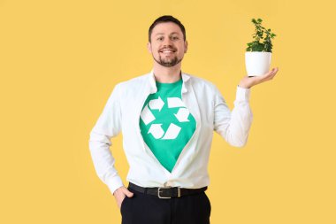 Geri dönüşüm işaretli tişörtlü genç adam ve sarı arka planda ev bitkisi. Ekoloji kavramı