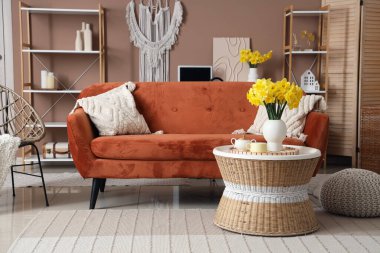 Kahverengi kanepesi, sehpası ve narsisli çiçekleri olan güzel bir oturma odası.