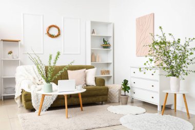 Yeşil kanepe, sehpa ve açık salonda çiçek açan dalları olan vazo.