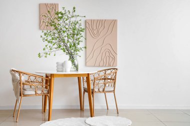 Masa, koltuklar ve vazo. Güzel yemek odasındaki beyaz duvarın yanında çiçek açan dallar.