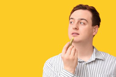 Sarı arka planda dudak kremi süren yakışıklı genç adam.