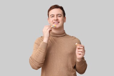 Gri arkaplanda dudak merhemi olan yakışıklı bir genç.