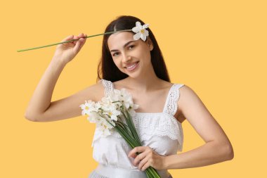 Sarı arka planda beyaz nergis çiçekleri olan mutlu genç bir kadın.