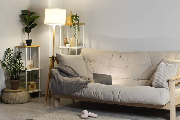 Interior of living room with sofa, glowing lamp and shelf units at night