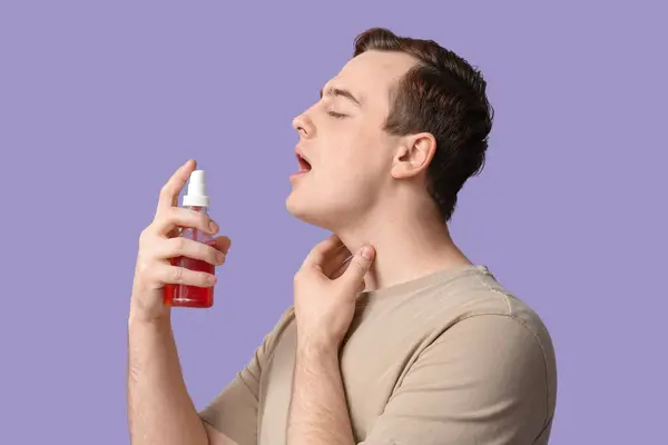 Young Man Sore Throat Spray Lilac Background Imagen de archivo
