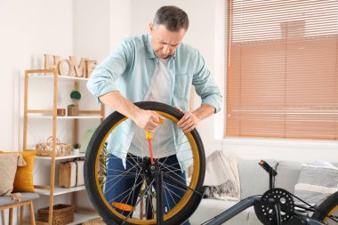 Evde tornavidayla bisiklet tekerleğini tamir eden olgun bir adam.