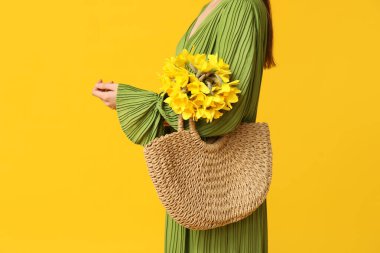 Hasır çantalı güzel bir kadın ve sarı arka planda güzel narsisli çiçekler, yakın plan.
