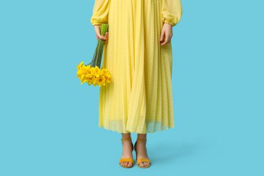 Mavi arka planda güzel narsisli çiçeklerle dolu buketi olan güzel genç bir kadın, yakın plan.