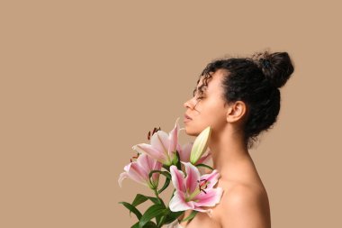 Bej arka planda pembe zambak çiçekleri olan güzel bir Afro-Amerikalı kadın.