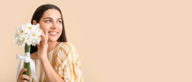 Beyaz nergis çiçekli mutlu genç kadın bej arka planda ve metin için yeri var