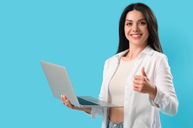 Diz üstü bilgisayarı olan kadın programcı mavi arka planda başparmağını kaldırıyor