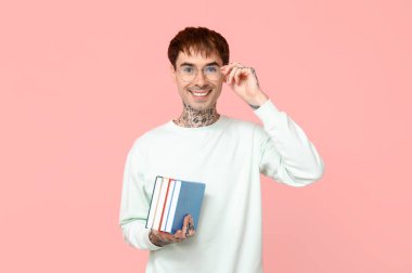 Pembe arka plan kitapları olan dövmeli genç bir adam.