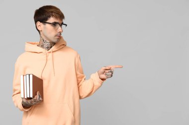 Gri arka plandaki bir şeyi gösteren kitapları olan dövmeli genç bir adam.