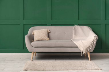 Yeşil duvarın yanında yastıklı ve battaniyeli modern gri kanepe