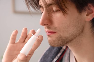 Hasta genç adam evde burun damlası kullanıyor, yakın plan.